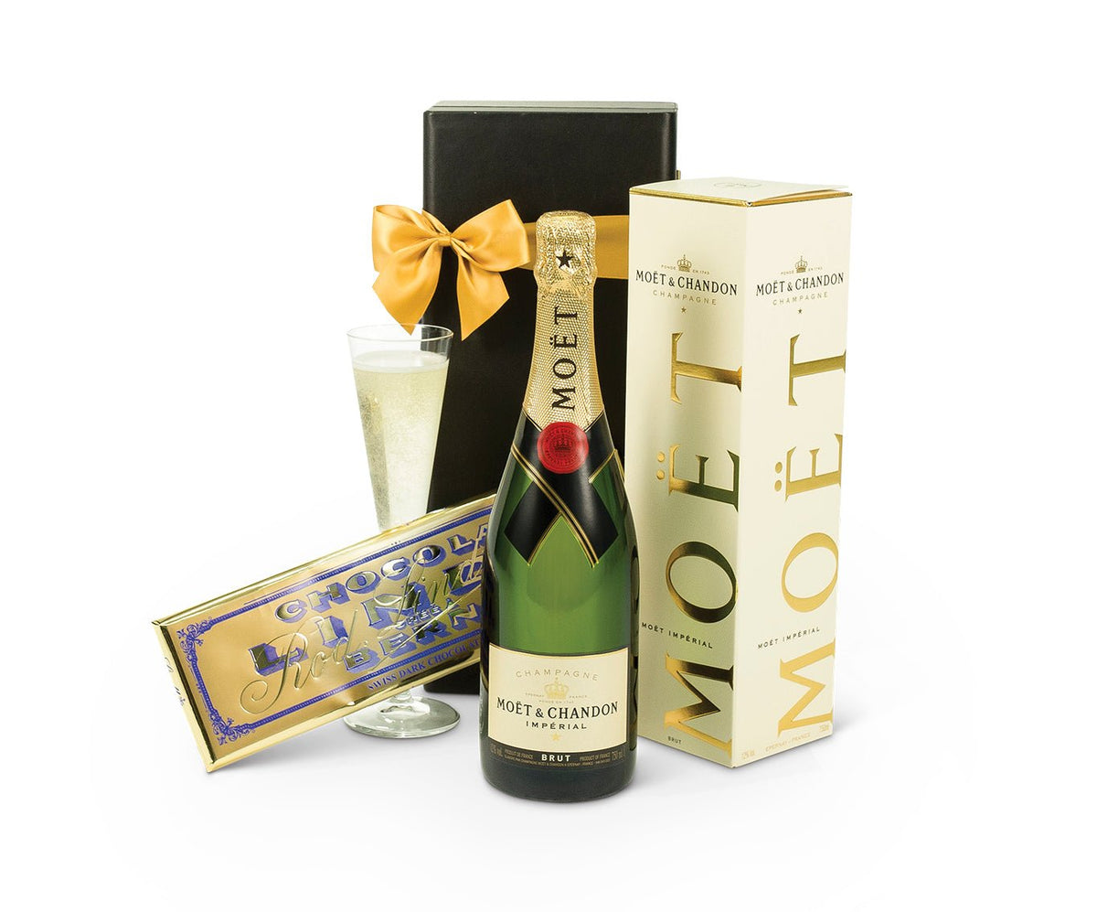 bottle of Moet with a bar of chocolate in front of a gift box with a golden ribbon and bow