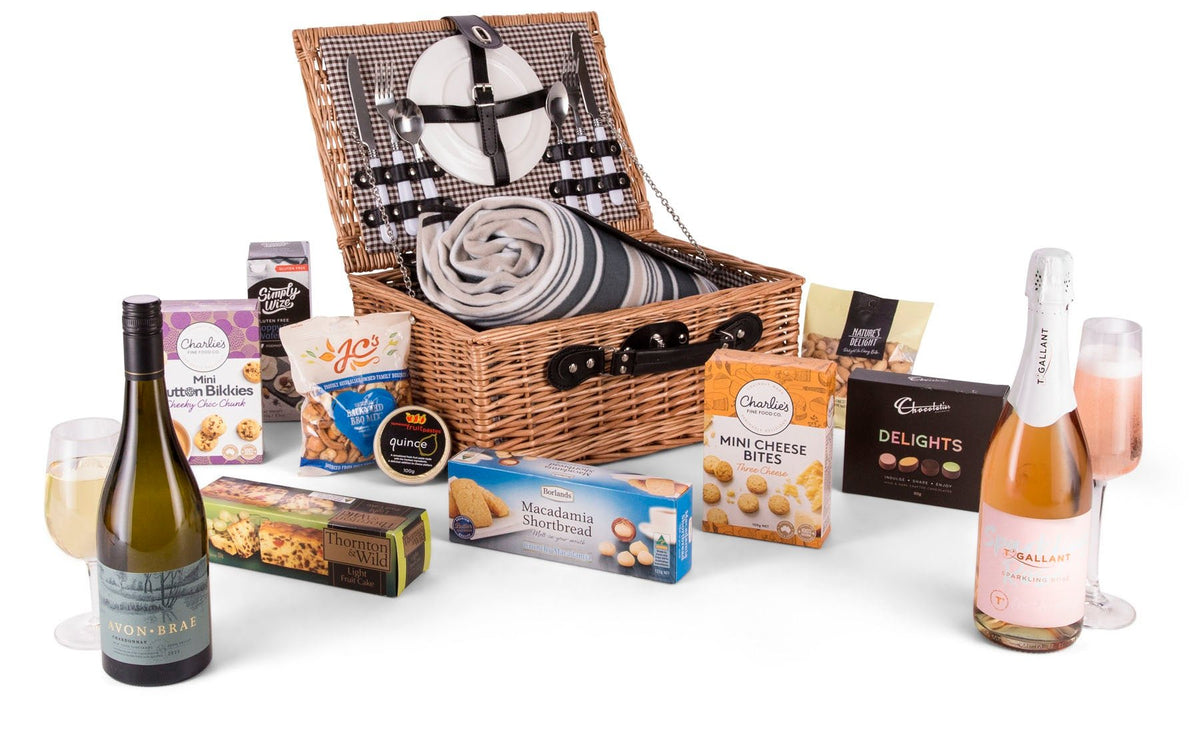 wicker picnic basket open to show picnic blanket and picnic set with wine and treats in front